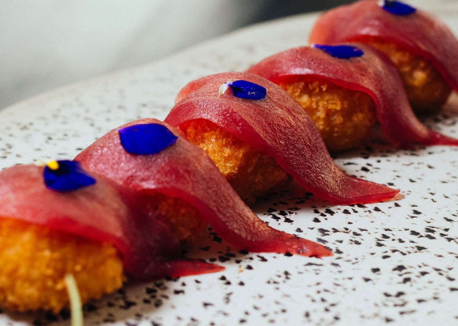 Golden prawn croquettes with slices of bluefin tuna sashimi and blue petals on a white plate