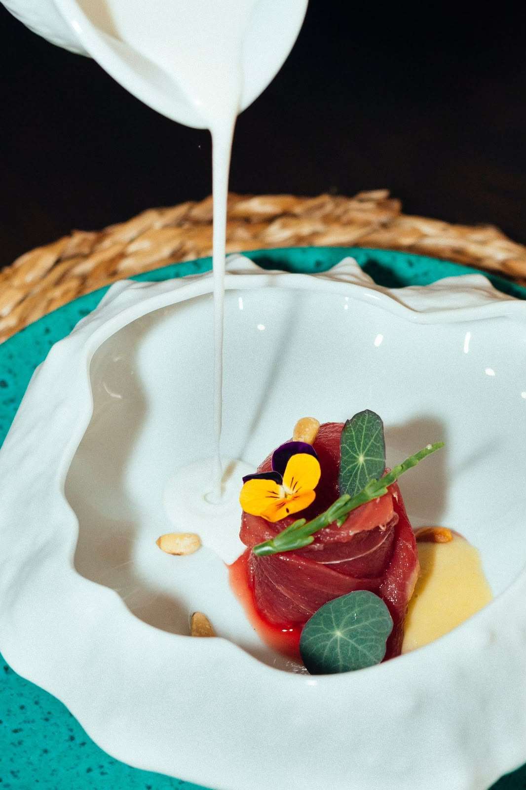 Ajoblanco poured beside bluefin tuna with leaves and flowers in a white bowl