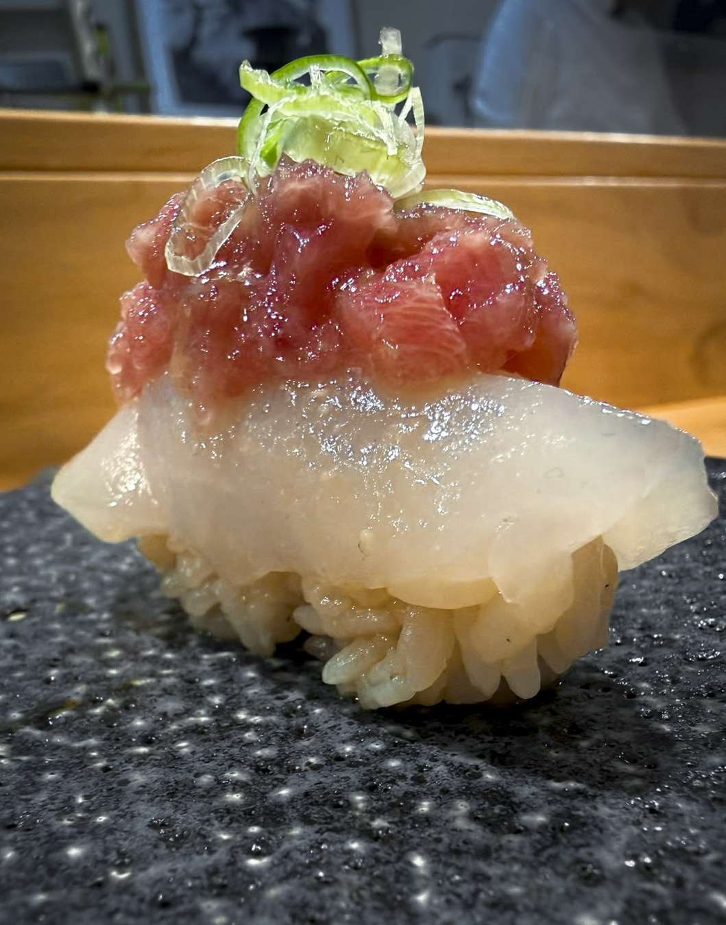 Close-up of a scallop nigiri topped with chutoro tartare and sprouts